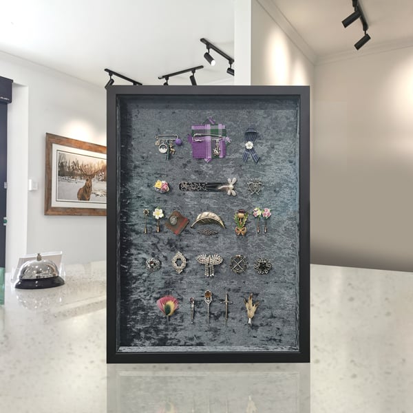 An eclectic collection of multiple brooches framed on a velvet backing in a complex arrangement.