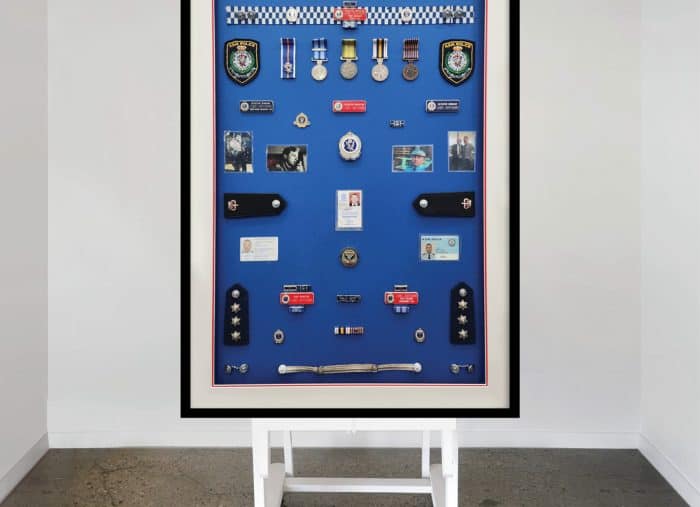 A comprehensive collection of police memorabilia including pins, badges, cards, photos and uniform attachments framed