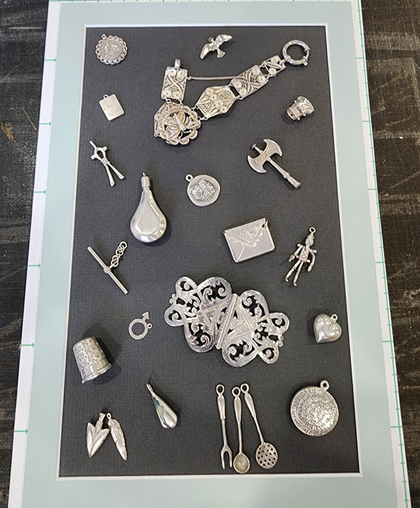 A collection of bracelet charms framed for a client.